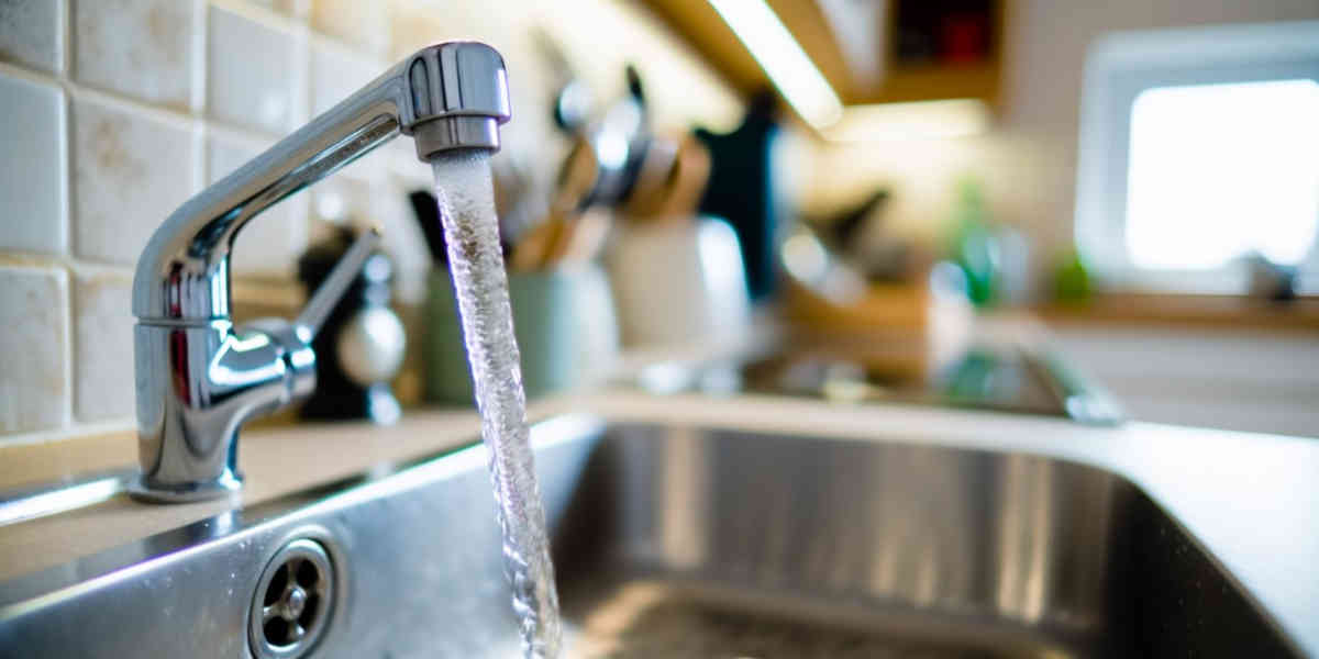 Close-up of a modern chrome kitchen faucet with water running into a stainless steel sink.